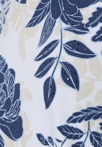 Kurzärmeliges Stoffhemd mit floralen Mustern in Marineblau und Beige, versehen mit glänzenden Akzenten auf den Blättern und einer weichen Textur vor einem hellen Hintergrund.