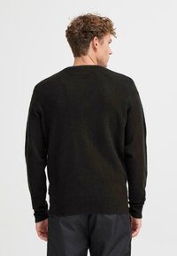 Mørkegrønn, teksturert strikkegenser med lange ermer og rund hals. Ribbestrikkede mansjetter og nederkant, med et avslappet passformdesign.