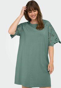 Rochie din bumbac verde, cu mâneci scurte decorate cu dantelă florală, decolteu rotund și croială lejeră, ce ajunge deasupra genunchiului.