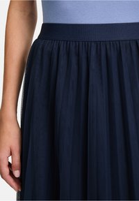 Gonna in tulle di colore navy con vita arricciata e strati di tessuto trasparente. Il materiale sembra leggero e fluido.