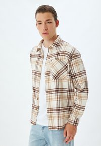 Geruite overhem shirt in crèmekleur, bruin en tan; flanellen materiaal met een borstzak; relaxed fit; gecombineerd met een wit t-shirt.