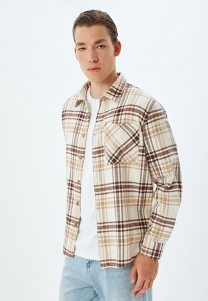 Camisa de cuadros en crema, marrón y tostado; material de franela con un bolsillo en el pecho; corte relajado; combinada con una camiseta blanca.