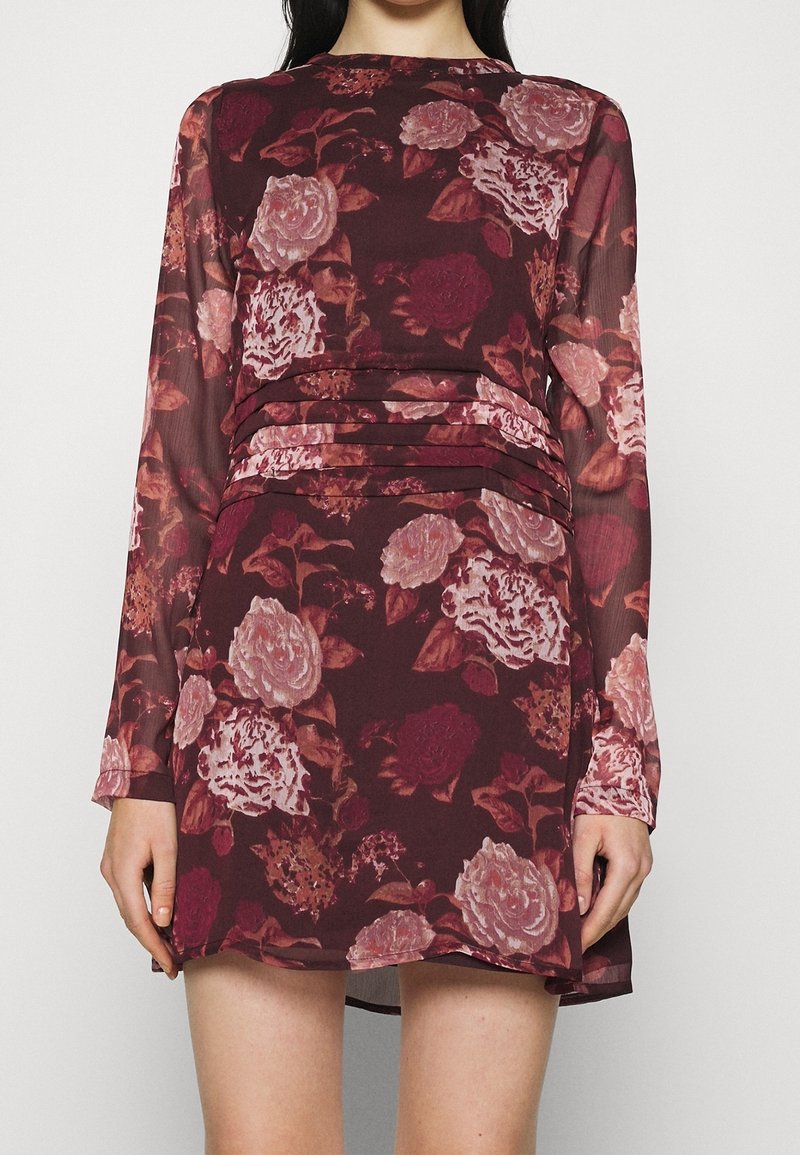 Långärmad klänning i bordeauxfärgad tyg med blommönster i nyanser av rosa och mörkröd, med rynkad midja och lager-på-lager textur.
