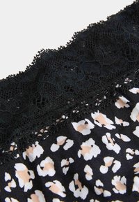 Schwarze Spitzenbordüre auf einem Stoff mit beigem, weißem und schwarzem abstraktem Leopardenmuster.