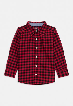 Chemise à carreaux rouges et noirs, à manches longues et boutonnée, avec un col pointu et des poches poitrine, présentée sur un fond uni.