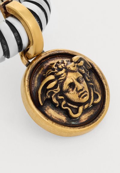 Pendentif rond en or avec un design en relief de tête de Méduse suspendu à un cordon rayé noir et blanc.