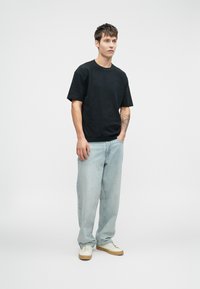 Μαύρο βαμβακερό μπλουζάκι, κοντό μανίκι, με λαιμόκοψη. Συνδυάζεται με ανοιχτό μπλε τζιν παντελόνι και λευκά αθλητικά παπούτσια με μπεζ λεπτομέρειες.