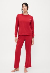 Rød bomullsloungewear sett bestående av en langermet topp med rund hals og avslappet passform, kombinert med rettbente bukser. Merkevaren synlig.