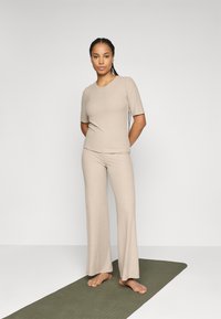 Ensemble de vêtements de détente beige en maille côtelée comprenant un haut ajusté à manches courtes et un pantalon évasé, fabriqué à partir d'un tissu doux au toucher lisse.