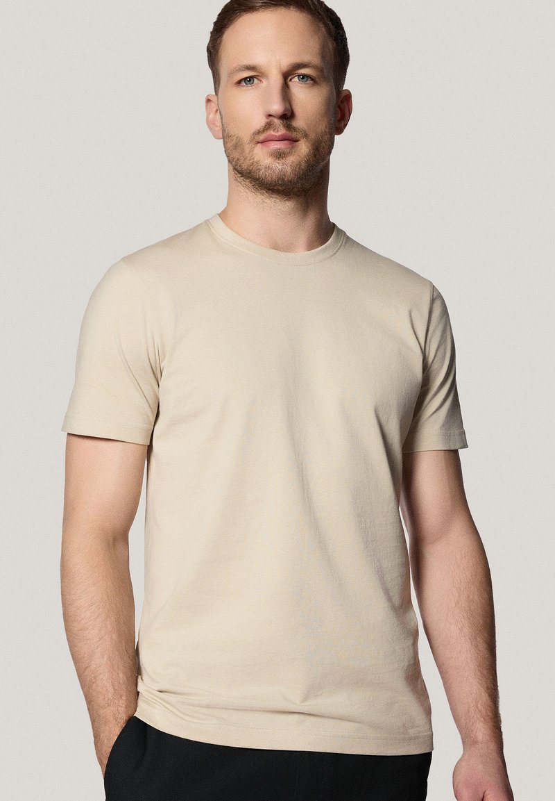 Beżowa koszulka krótki rękaw z miękkiej bawełny, z klasycznym okrągłym dekoltem i luźnym krojem, o minimalistycznym wzornictwie bez widocznych wzorów.