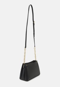 Bolso de cuero negro texturizado con una forma estructurada, que cuenta con un asa de cadena dorada y una correa de hombro negra ajustable y delgada.