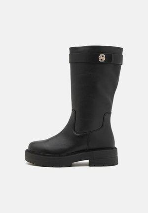 Sorte knelange støvler med en glat læderfinish, en kraftig sål og et dekorativt bånd med et guld logo-accent.