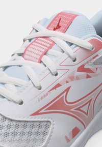 Λεπτομερής εικόνα αθλητικού παπουτσιού σε λευκό και ροζ με κορδόνια μπροστά, πλέγμα στη μύτη και σχέδιο με λογότυπο στην πλευρά και τη γλώσσα.