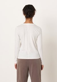 Pikad varrukad, helehall ülaosa ümarate kaelustega, millel on keskjoon ja pehme tekstuur, kombineeritud kõrge vöökohaga pruunide pükstega.