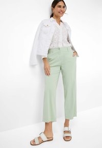 Lichtgroene, cropped pantalons met een rechte pasvorm, gecombineerd met een doorschijnende witte blouse met bloemenprint en een witte denimjack. Witte sandalen maken de look compleet.