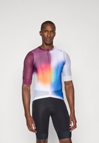 Maillot de cyclisme à manches courtes avec un dégradé de violet à bleu, présentant une texture en maille et une fermeture éclair à l'avant, associé à un short de cyclisme noir.