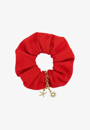 Czerwona teksturowana gumka do włosów z złotym łańcuszkiem ozdobionym zawieszkami w kształcie rozgwiazdy i słońca na białym tle.