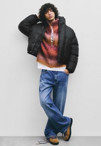 Czarna kurtka puchowa w połączeniu z gradientowym pomarańczowo-różowym swetrem, niebieskimi luźnymi dżinsami i brązowymi teksturowanymi butami.