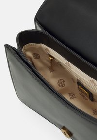 Zwarte leren tas met een gladde buitenkant, contrasterende beige stofvoering met een subtiel patroon. Bevat een ritsvak en bronzen hardware.