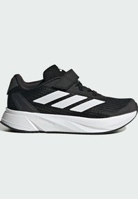 Zapatilla deportiva negra con parte superior de malla, rayas blancas y correa ajustable. Presenta una suela acolchada y tela texturizada para mayor soporte.