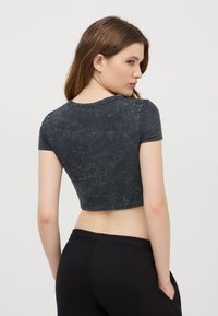 T-shirt nera cropped con maniche corte, caratterizzata da una texture marmorizzata e un collo rotondo. Abbinata a pantaloni neri, che presentano una vestibilità comoda.