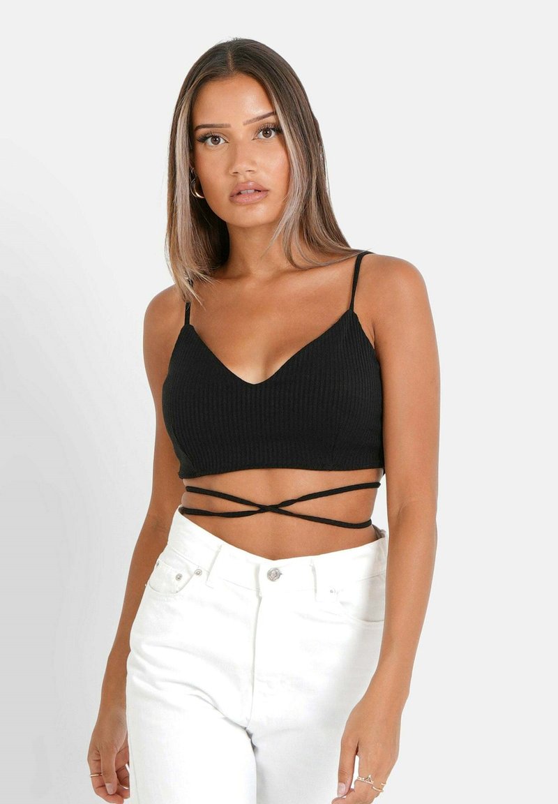 Top corto nero a costine con scollo a V e spalline sottili, con dettagli incrociati nella parte inferiore. Abbinato a jeans bianchi a vita alta.