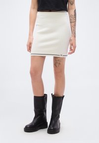 Λευκή  μίνι φούστα με υφή, με μαύρη και λευκή ζώνη στη μέση και τελείωμα, σε συνδυασμό με μαύρες μπότες μέχρι το γόνατο.