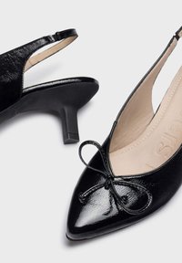 Talons hauts en cuir verni noir, avec un bout pointu, un accent en nœud à l'avant et un talon effilé. Texture lisse avec une finition brillante.