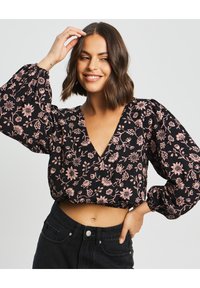 Čierny kvetinový crop top s hlbokým V-vznikom, dlhými nadúvanými rukávmi a vzorom ružových kvetov. Tkanina pôsobí ľahko a má mierne textúrovaný povrch.