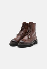 Bottes en cuir embossé crocodile marron avec un design à lacets, des détails de brogue décoratifs et une semelle noire robuste. Comprend une étiquette en argent.