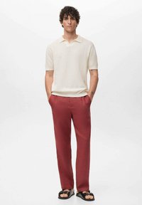 Cream textured polo shirt, burgundy pants, and black sandals. Simple design, short sleeves, and a classic collar.
