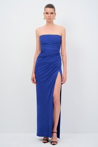 Strapless blaues Maxikleid mit drapiertem Stoff, ausgestattet mit einem hohen Schlitz und glatter Textur. Getragen mit schwarzen Riemchenschuhen und goldenen Ohrringen.