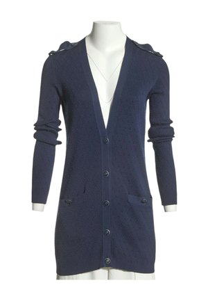 Cardigan long bleu marine en maille texturée, fermeture boutonnée, deux poches avant et détails de boutons aux épaules sur un mannequin blanc.