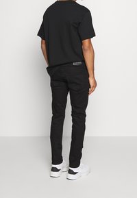 Svart bomull t-shirt med avslappnad passform, kombinerad med svarta slim-fit jeans och vita sneakers. Lätt textur, minimala accenter och inga synliga mönster.