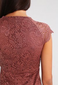 Bruine kanten jurk met ingewikkelde bloemenpatronen. Kapmouwen hebben een delicate kanten afwerking. De stof lijkt zacht met een lichte glans.