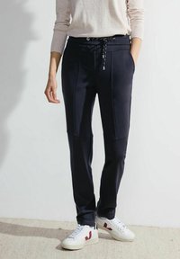 Marineblaue Jogginghosen mit taillierter Passform, elastischem Bund und kontrastierenden Nähten. Kombiniert mit weißen Sneakers mit roten Akzenten.