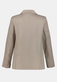 Veste beige cintrée avec un col cranté, des manches longues et un tissu texturé. Finition lisse et lignes épurées créent une silhouette structurée.