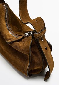 Borsa in suede marrone con dettagli neri, una cerniera argentata e una tracolla regolabile con due borchie metalliche.