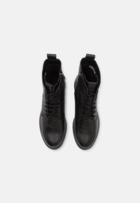 Bottes noires à la cheville avec un motif crocodile texturé, dotées d'une fermeture éclair latérale, d'un laçage à l'avant et d'une languette pour un enfilage facile. Semelle lisse.