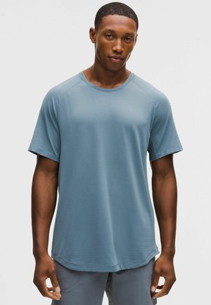 Lichtblauw atletisch T-shirt met korte mouwen, geribbelde textuur, ronde halslijn, licht aflopende zoom, gedragen met grijze broek.