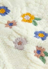 Țesătură crem tricotată cu broderie florală în albastru, portocaliu și maro, cu frunze verzi pe o suprafață texturată. Model distinctiv de cablu.