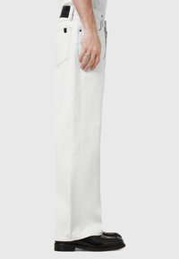 Hvide denimjeans med lige pasform, der har en sort læderpatch bagpå, parret med blanke sorte dressko.