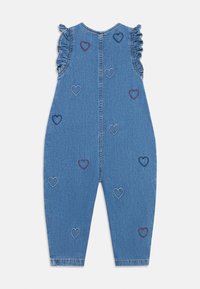 Džinsinis kombinezonas su raukinukais ant petnešėlių, mėlynos spalvos, siuvinėtais raudonais, tamsiai mėlynais ir baltais širdelėmis, su pilna nugaros dalimi ir tiesiomis kojų linijomis.