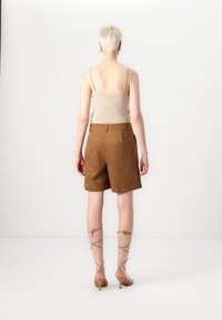 Shorts en daim marron avec une coupe décontractée, associés à un top beige ajusté. De longues sandales à talons couleur beige entourent les jambes, laissant la peau nue à découvert.