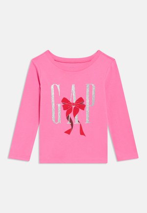 Rosa langärmeliges Kinderhemd mit silbernen Glitzerschriftzügen "GAP" und einem roten Schleifengrafik in der Mitte auf weißem Hintergrund.