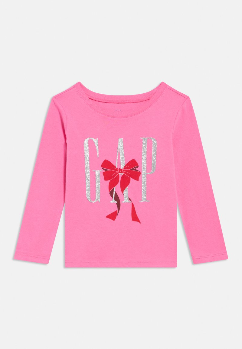 Rozā garroku bērnu krekls ar sudraba mirdzošiem burtiem "GAP" un sarkanu loku centrā uz baltas fona.