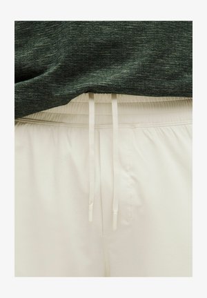 Šviesiai kreminės šortai su elastine juostele ir raišteliais, derinami su jautraus tamsiai žaliais marškiniais.