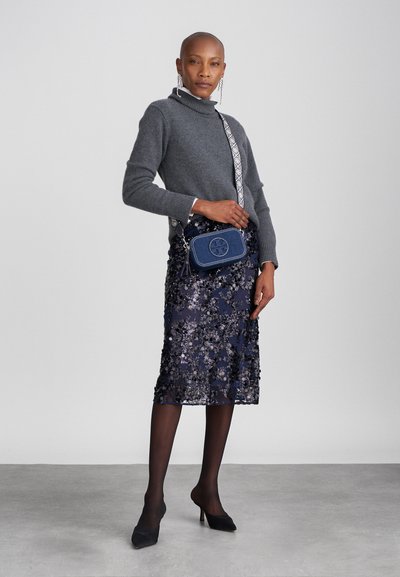 Sweater cinza de gola alta, saia azul marinha com lantejoulas, stiletto pretos, bolsa de denim cruzada texturizada com alça estampada, brincos prateados e meias finas.