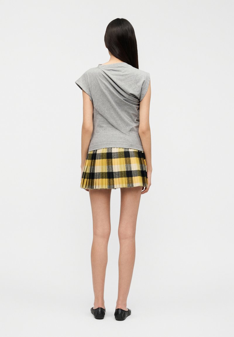Gray short-sleeve top with draped back paired with a yellow and black plaid pleated skirt, showcasing a layered design and distinct textures.
