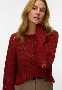 Maglione lavorato a maglia di un profondo rosso con motivi a giorno, collo rotondo e maniche lunghe; tessuto testurizzato e vestibilità leggermente ampia.